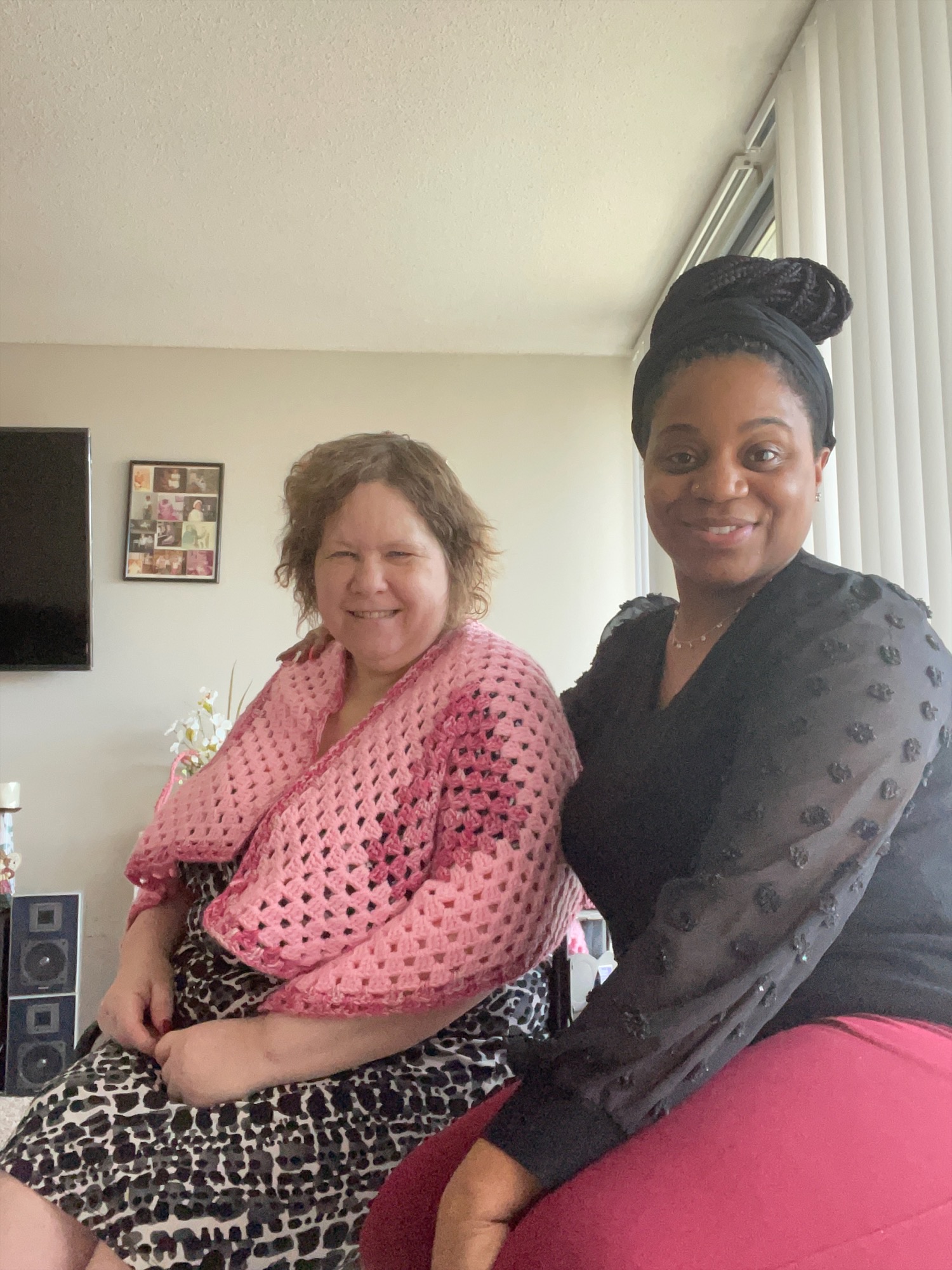 Two women sit side by side in an apartment smiling