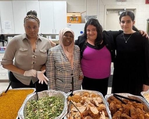 Four women standing behind trays of Thanksgiving food